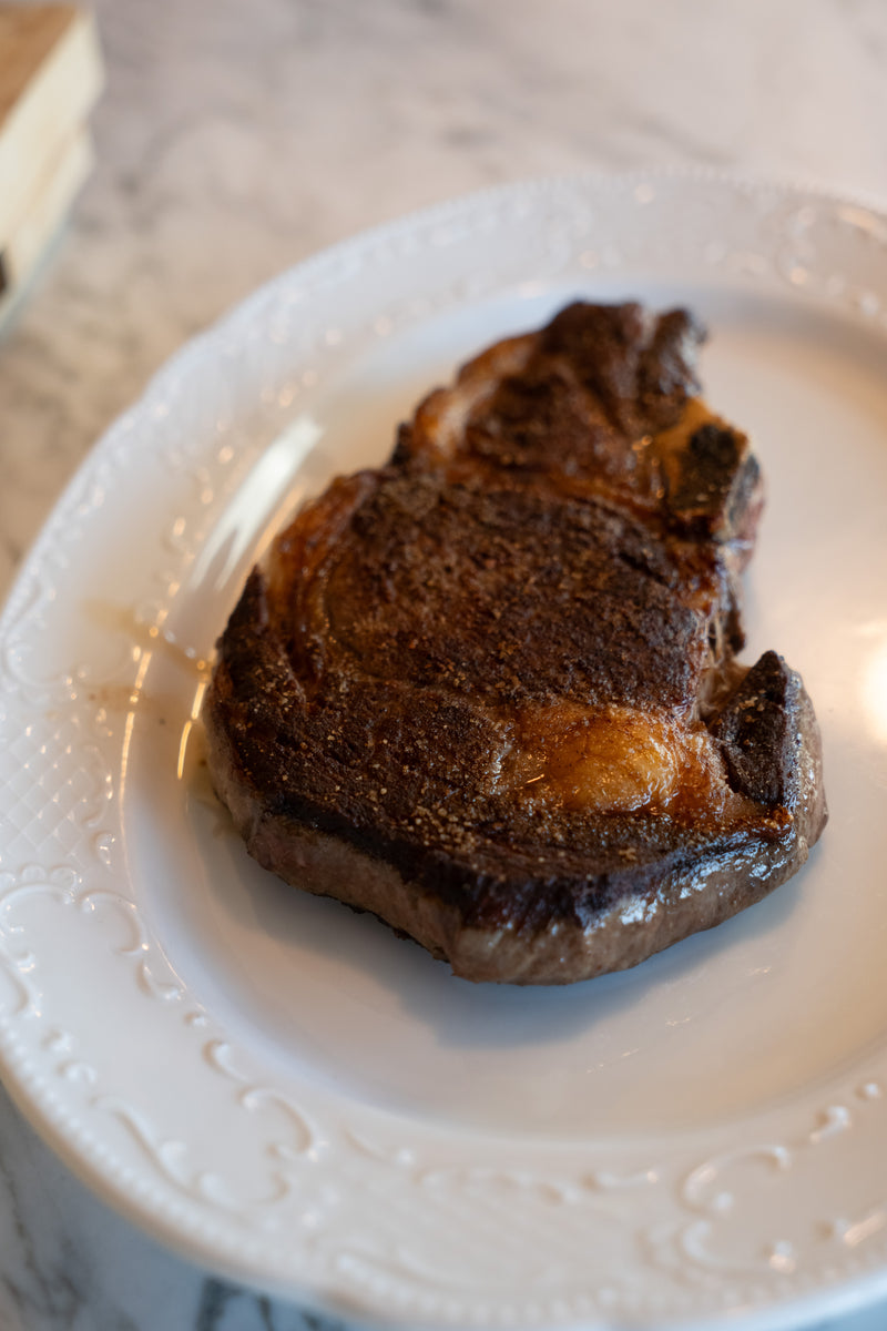 Grilled New England Wagyu steak on a white plate with a marble countertop background